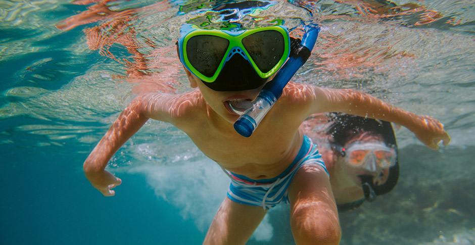 Child learning to snorkel with his mother in sea.